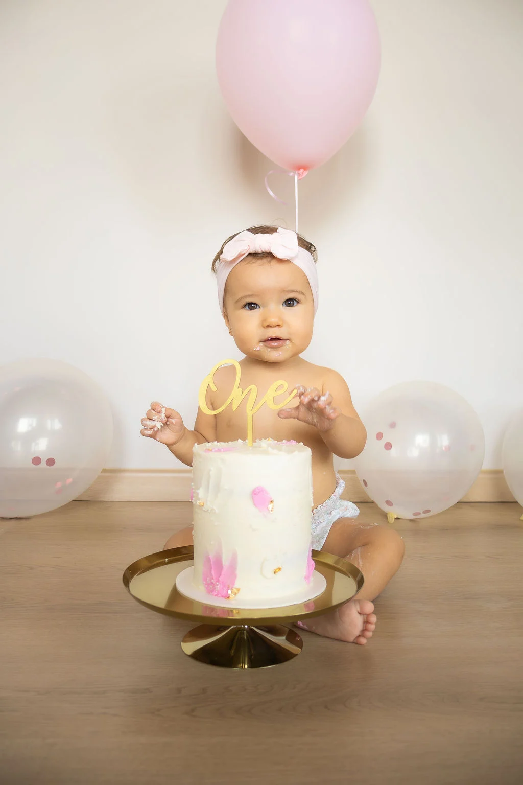 Bebé celebrando su primer cumpleaños con pastel y globo rosa