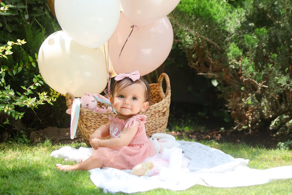 Bebé en un jardín con globos de cumpleaños